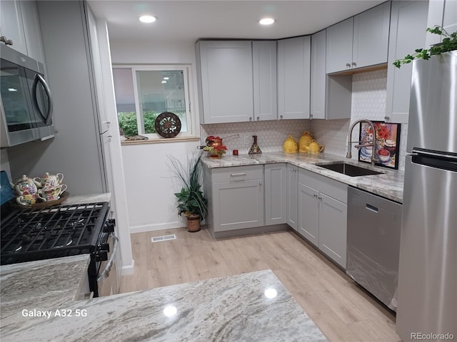 kitchen featuring visible vents, appliances with stainless steel finishes, light stone countertops, gray cabinetry, and a sink