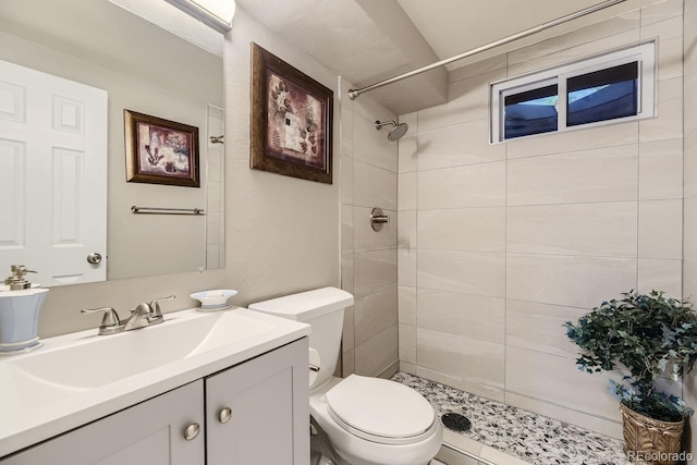 bathroom featuring toilet, tiled shower, and vanity