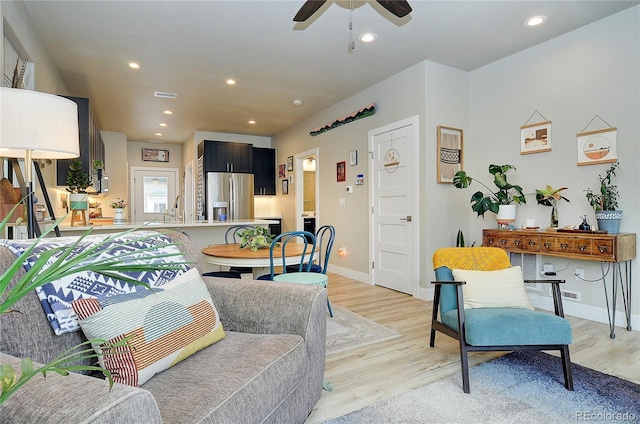 living room featuring light wood-type flooring, ceiling fan, and sink