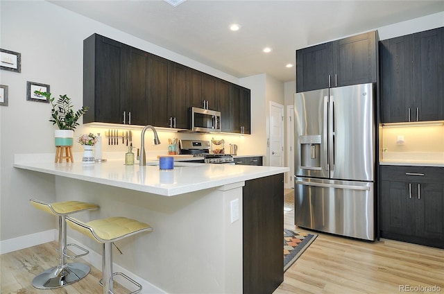 kitchen featuring sink, a kitchen breakfast bar, light hardwood / wood-style flooring, kitchen peninsula, and appliances with stainless steel finishes