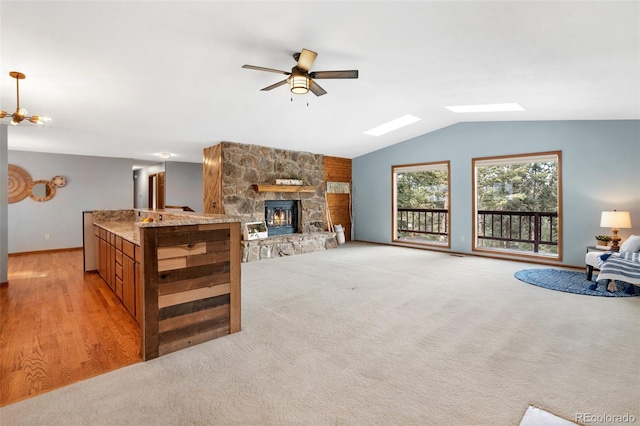 living room with ceiling fan, vaulted ceiling with skylight, light colored carpet, and a fireplace