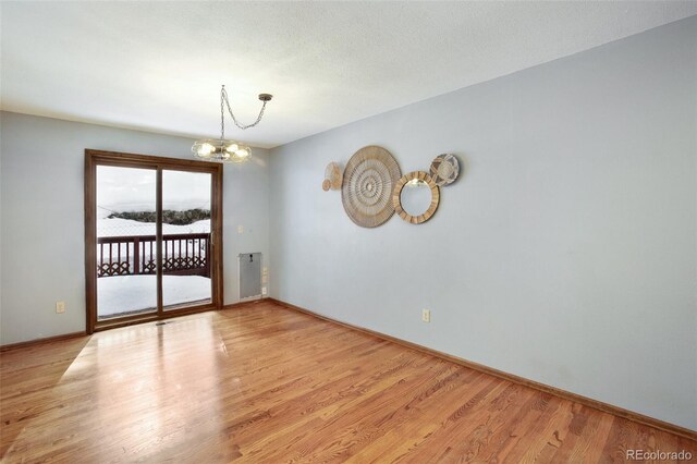 unfurnished room featuring an inviting chandelier, a textured ceiling, and light wood-type flooring