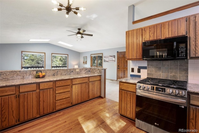 kitchen featuring lofted ceiling, stainless steel gas range oven, light hardwood / wood-style floors, ceiling fan with notable chandelier, and backsplash