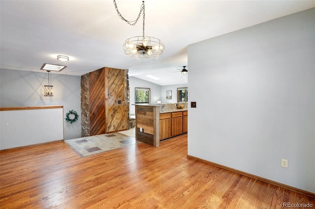 kitchen with pendant lighting, light stone counters, vaulted ceiling, kitchen peninsula, and light wood-type flooring