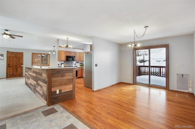 kitchen featuring appliances with stainless steel finishes, ceiling fan with notable chandelier, pendant lighting, light stone countertops, and light hardwood / wood-style flooring