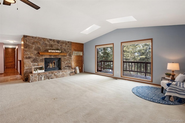 living room featuring ceiling fan, a fireplace, carpet flooring, and lofted ceiling with skylight