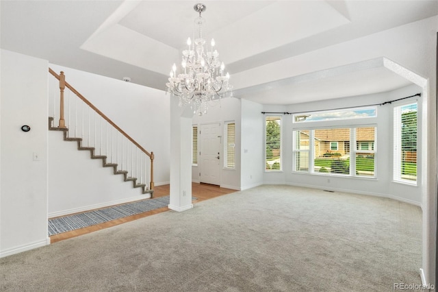 unfurnished living room featuring light carpet, a chandelier, and a raised ceiling