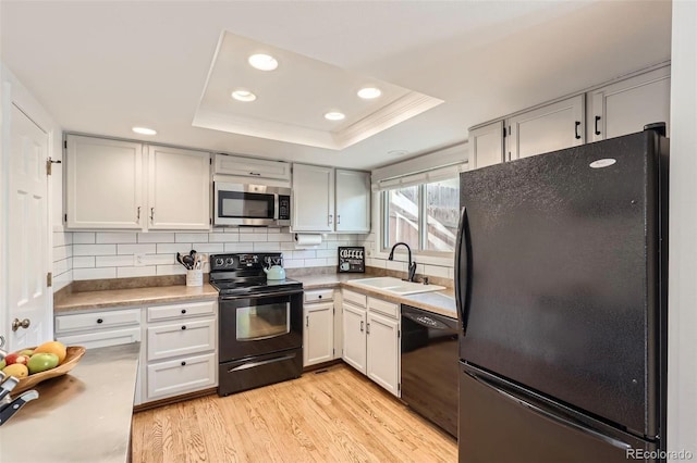 kitchen with sink, a tray ceiling, black appliances, and white cabinets