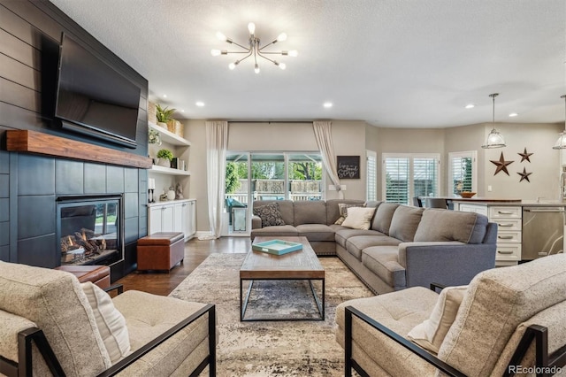 living room featuring recessed lighting, a chandelier, wood finished floors, a tiled fireplace, and a textured ceiling
