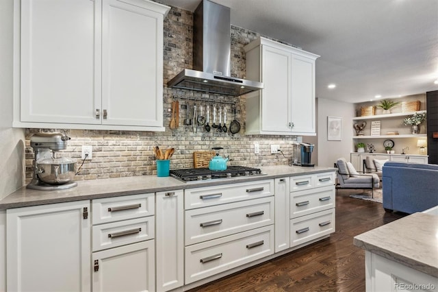 kitchen featuring wall chimney range hood, stainless steel gas stovetop, dark wood finished floors, decorative backsplash, and white cabinets