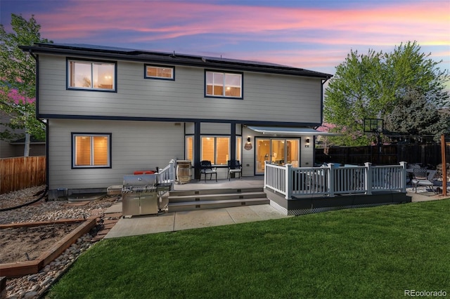 back of property at dusk featuring a deck and roof mounted solar panels