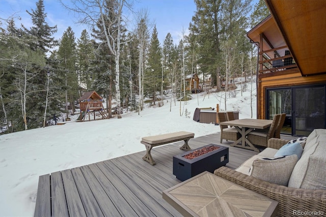 snow covered deck featuring a hot tub, a playground, and a fire pit