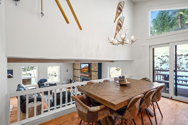 dining area featuring hardwood / wood-style flooring, an inviting chandelier, a towering ceiling, plenty of natural light, and a fireplace