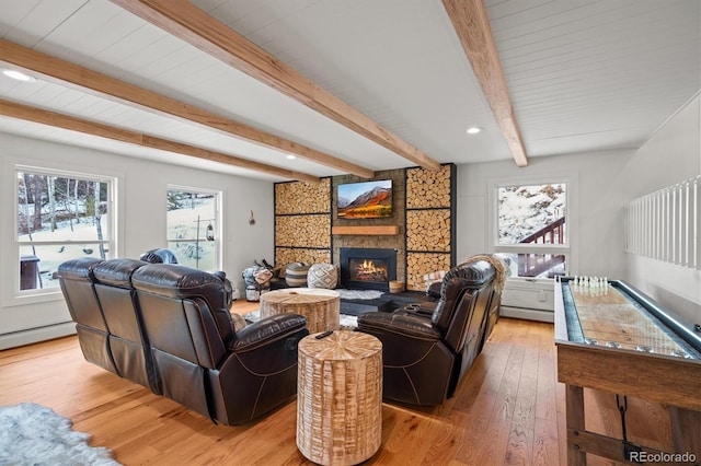 living room featuring beamed ceiling, a large fireplace, a baseboard radiator, and light hardwood / wood-style flooring