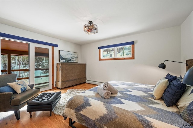 bedroom with a baseboard radiator, access to exterior, light hardwood / wood-style floors, and multiple windows