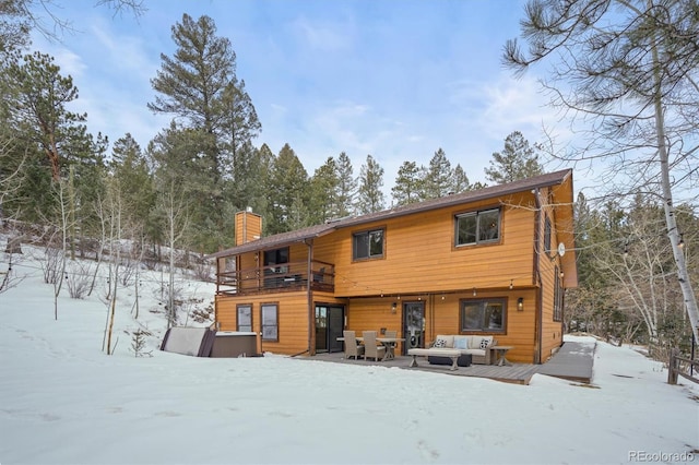 snow covered back of property with a balcony and outdoor lounge area