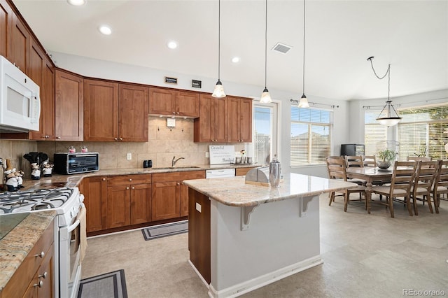 kitchen featuring white appliances, a kitchen island, pendant lighting, light stone counters, and a breakfast bar area