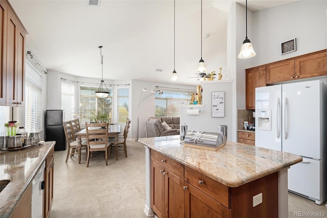 kitchen featuring a center island, light stone countertops, decorative light fixtures, and white appliances