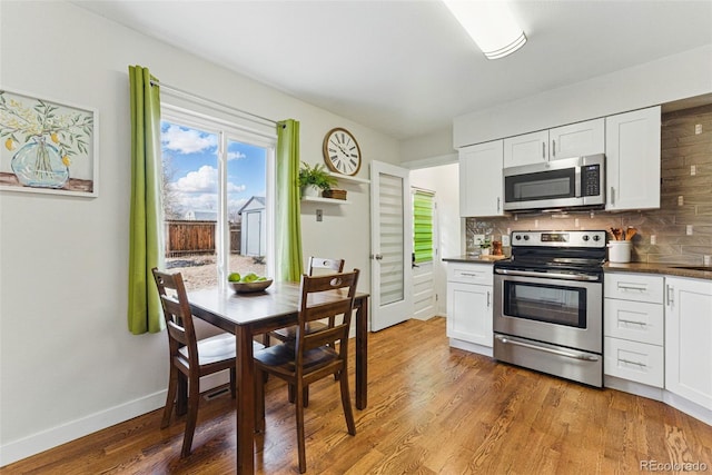 kitchen featuring dark countertops, light wood-style flooring, decorative backsplash, appliances with stainless steel finishes, and white cabinetry