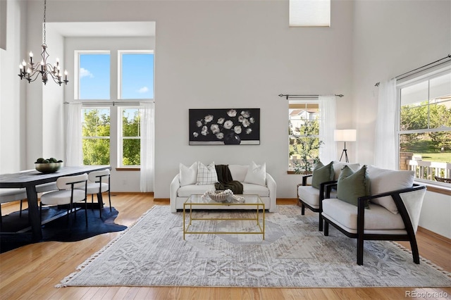 living room featuring a towering ceiling, a chandelier, plenty of natural light, and wood finished floors