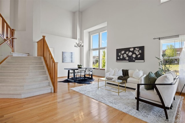 living area featuring stairs, a towering ceiling, a chandelier, wood finished floors, and baseboards