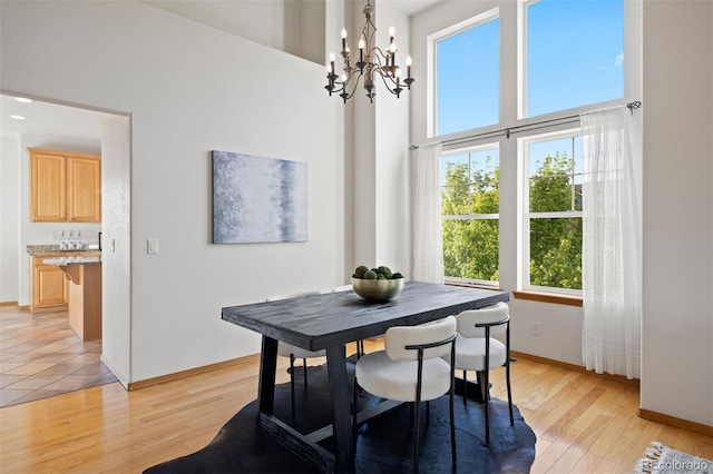dining area with a chandelier, light wood finished floors, a towering ceiling, and baseboards