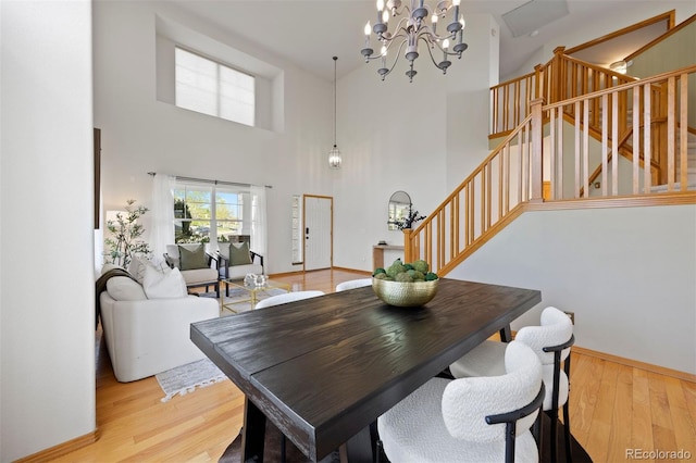 dining area with a chandelier, stairway, light wood-type flooring, a high ceiling, and baseboards