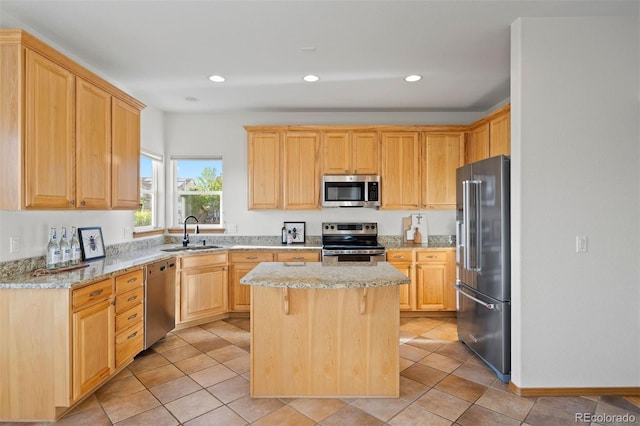 kitchen featuring stainless steel appliances, a sink, light brown cabinetry, a kitchen island, and light stone counters