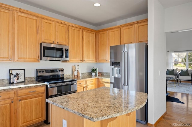 kitchen featuring appliances with stainless steel finishes, light stone countertops, a kitchen island, and recessed lighting