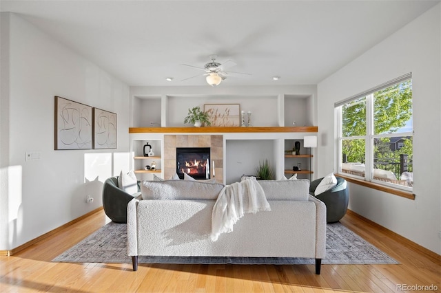 living area with built in features, wood finished floors, ceiling fan, and a fireplace