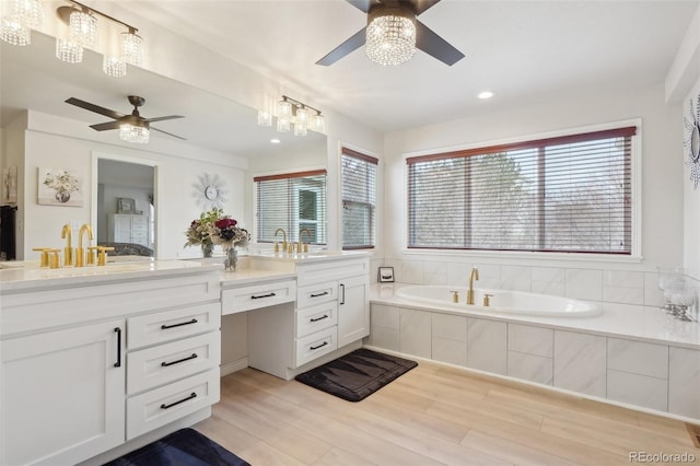 bathroom with hardwood / wood-style flooring, vanity, ceiling fan, and tiled tub