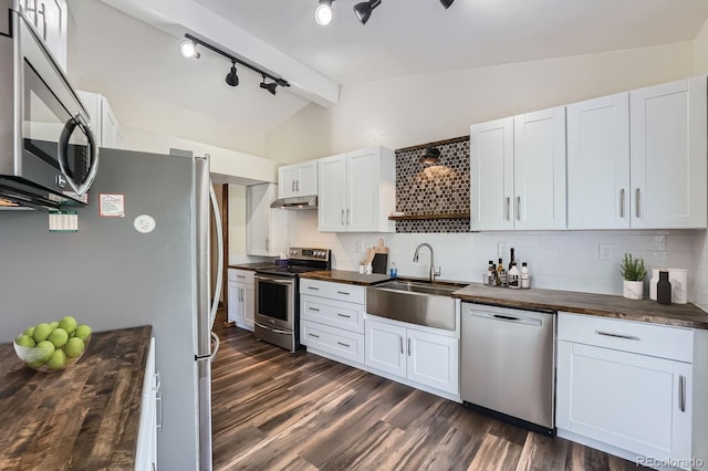 kitchen with appliances with stainless steel finishes, lofted ceiling with beams, a sink, butcher block countertops, and under cabinet range hood