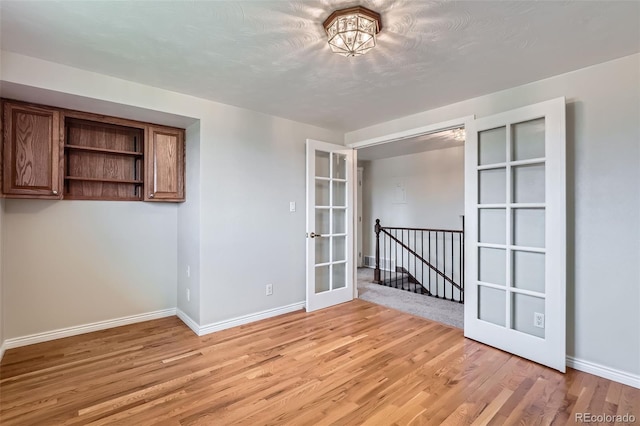 spare room with french doors, light wood-style floors, and baseboards