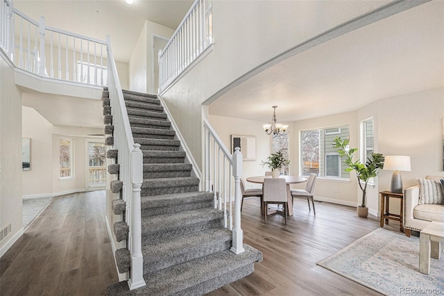 foyer with a high ceiling, wood finished floors, baseboards, stairway, and an inviting chandelier