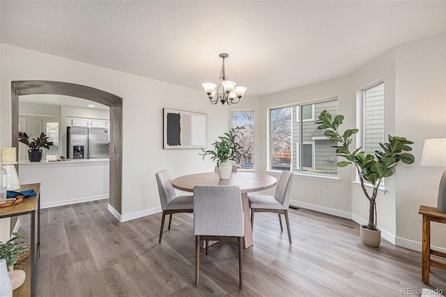 dining room with a chandelier, arched walkways, baseboards, and wood finished floors