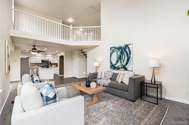 living area with arched walkways, a ceiling fan, a towering ceiling, stairs, and baseboards