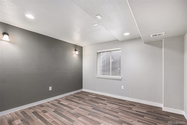 empty room with visible vents, a textured ceiling, baseboards, and wood finished floors