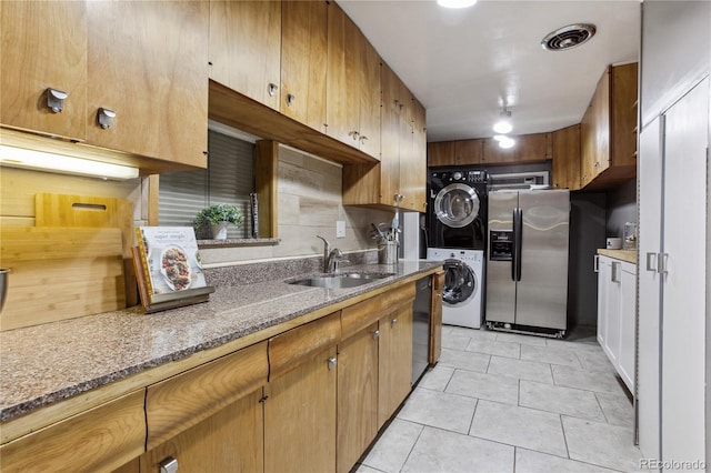 kitchen featuring stacked washer and dryer, sink, light tile patterned floors, stainless steel fridge, and black dishwasher