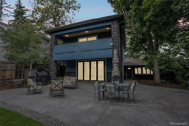 back house at dusk with a balcony, an outdoor living space, and a patio