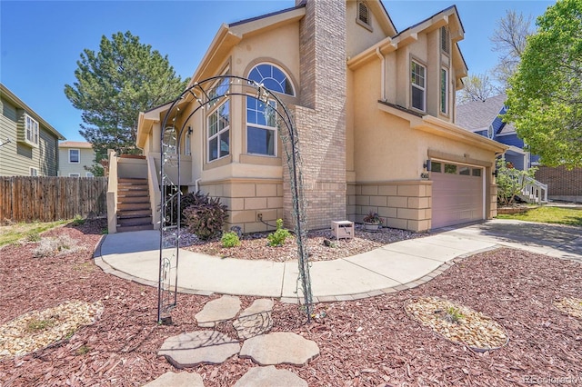 view of front facade featuring stucco siding, a garage, a chimney, fence, and concrete driveway