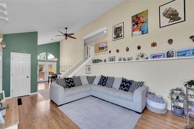 living area with wood finished floors, ceiling fan, stairway, french doors, and high vaulted ceiling