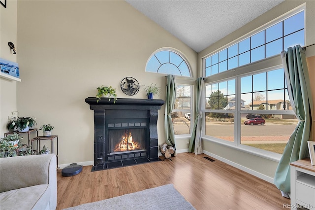 living room with wood finished floors, a textured ceiling, a fireplace with flush hearth, baseboards, and high vaulted ceiling