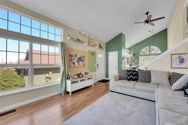 living room with ceiling fan, high vaulted ceiling, wood finished floors, baseboards, and a textured ceiling