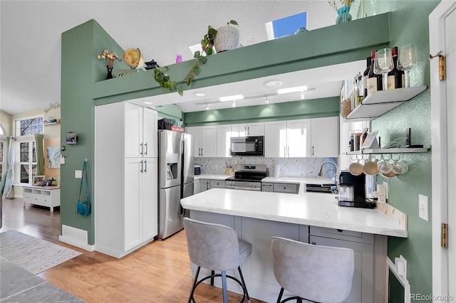 kitchen featuring appliances with stainless steel finishes, a peninsula, open shelves, white cabinetry, and healthy amount of natural light