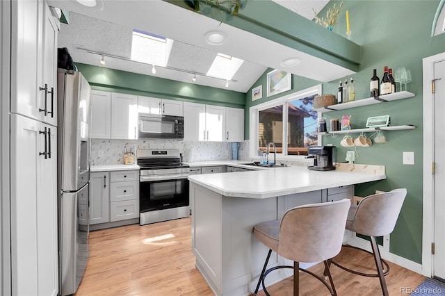 kitchen with appliances with stainless steel finishes, a peninsula, a skylight, a sink, and tasteful backsplash