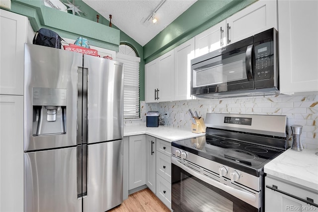 kitchen with appliances with stainless steel finishes, a textured ceiling, lofted ceiling, tasteful backsplash, and white cabinets