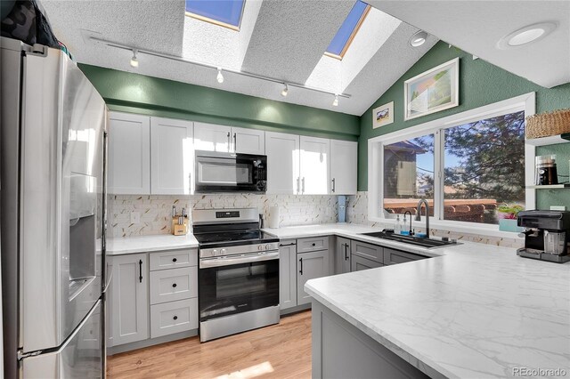 kitchen featuring appliances with stainless steel finishes, a skylight, a sink, rail lighting, and decorative backsplash