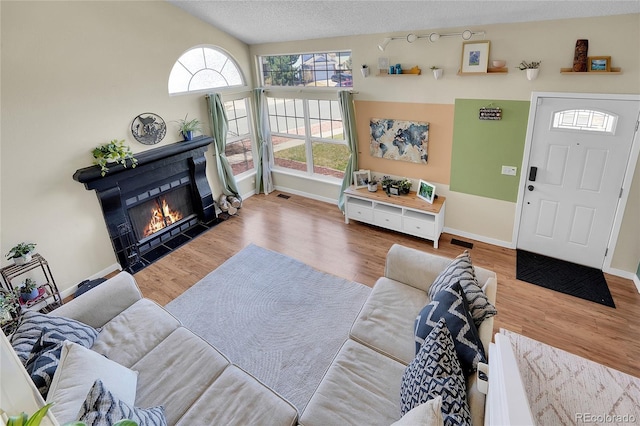 living room with a tiled fireplace, wood finished floors, baseboards, vaulted ceiling, and a textured ceiling
