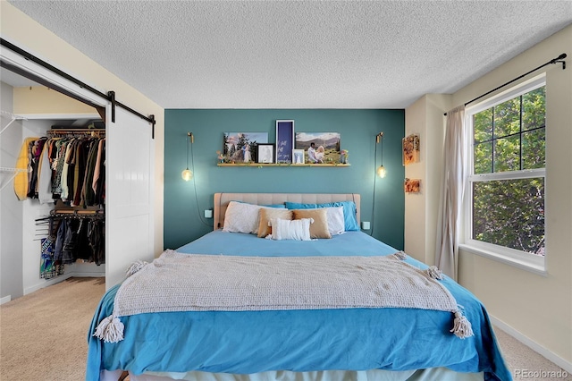 carpeted bedroom featuring a barn door, a textured ceiling, baseboards, and a closet