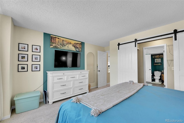 bedroom featuring a barn door, light colored carpet, a textured ceiling, and baseboards